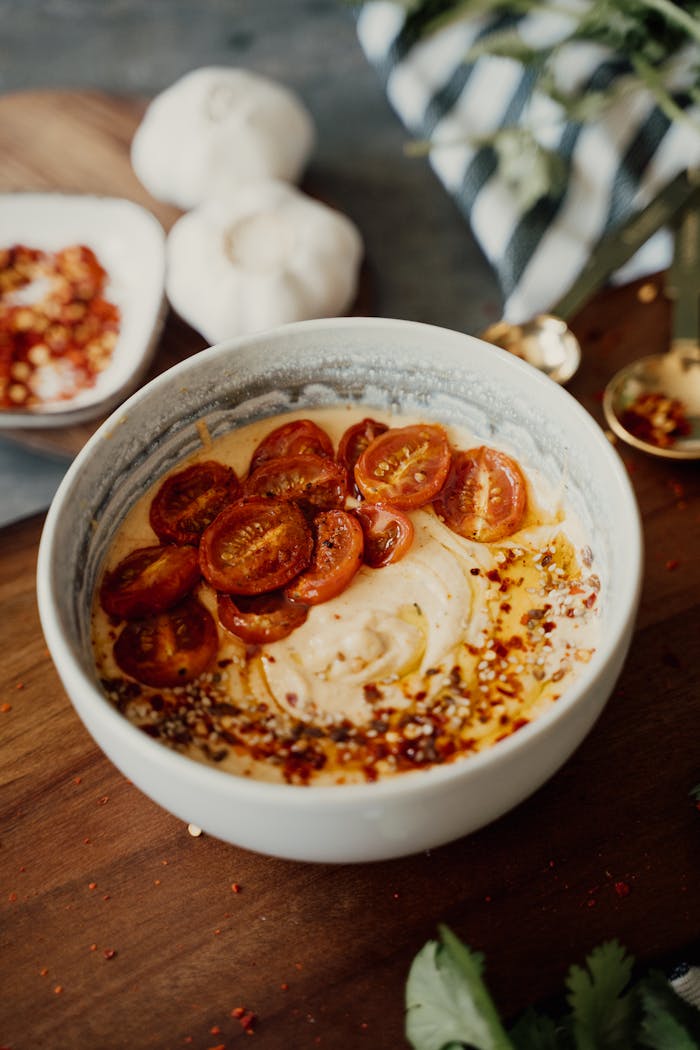 services-03 Delicious bowl of creamy hummus topped with cherry tomatoes and spices on a rustic wooden table.