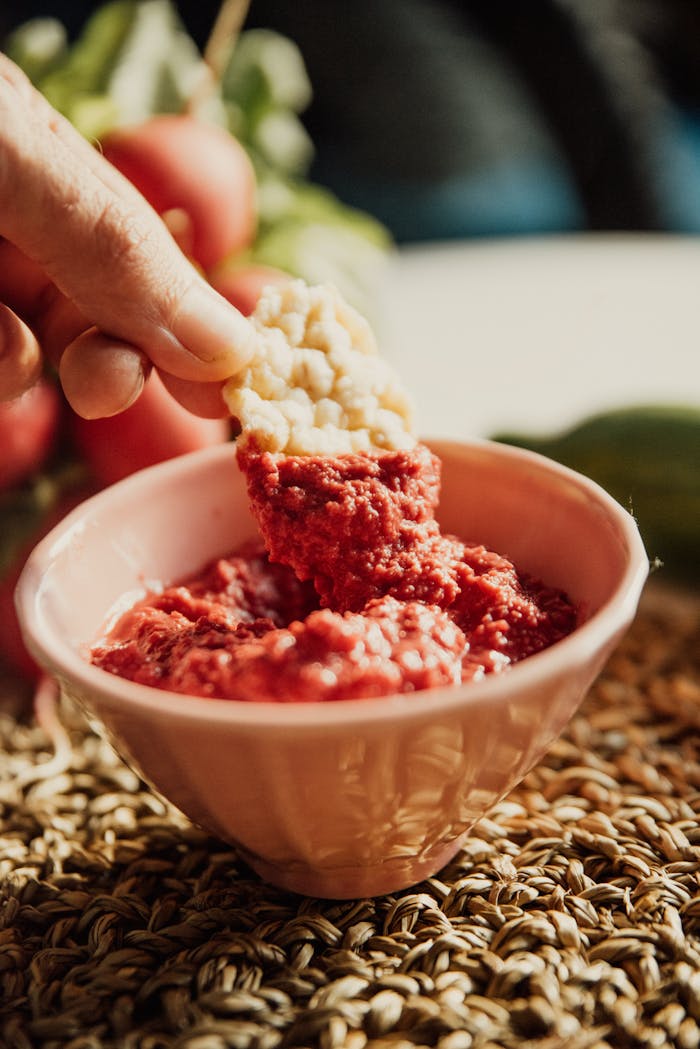 A person dipping crispbread into a bowl of fresh red beet hummus.